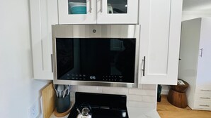 A kitchen with a stainless steel microwave, white cabinets, and a black stove.