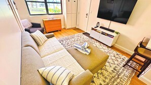 A living room with a sofa, a TV, a bookshelf, and a window with a view.