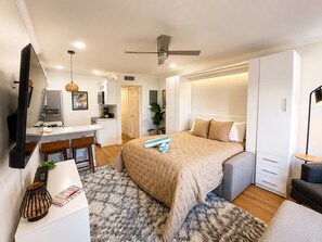 Une chambre d’hôtel moderne équipée d’un lit, d’un bureau, d’une kitchenette et d’un ventilateur de plafond.