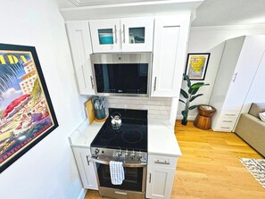 A compact kitchen with white cabinets, a microwave, a stove, and a sink.