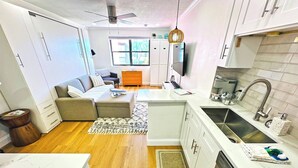 A compact kitchen with white cabinets, a stainless steel sink, and a modern ceiling fan.