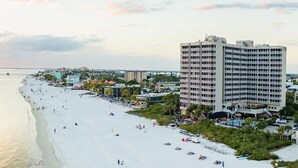 A beachfront hotel with multiple floors, a pool area, and a beach in the background. - Beach Vacay With View! Direct Beach Access, Pool, Bar, Restaurant! (Fort Myers Beach)