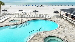 A pool area with lounge chairs and umbrellas, a beach in the background, and a bar area with seating. - Beach Vacay With View! Direct Beach Access, Pool, Bar, Restaurant! (Fort Myers Beach)