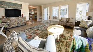 A spacious living room with a sofa, a coffee table, and a TV on a herringbone-patterned cabinet. - Beautifully updated cottage with ocean views, only steps to the beach! (Wrightsville Beach)