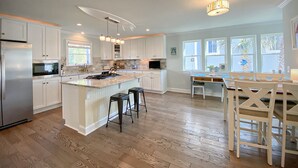 A spacious kitchen with white cabinetry, a central island with stools, and a dining area with a table and chairs. - Beautifully updated cottage with ocean views, only steps to the beach! (Wrightsville Beach)