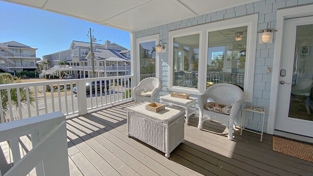 A covered porch with wicker furniture, glass doors, and a view of neighboring houses. - Beautifully updated cottage with ocean views, only steps to the beach! (Wrightsville Beach)