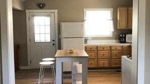 Een compacte keuken met een centraal kookeiland, houten kastjes, een koelkast en een raam dat voor natuurlijk licht zorgt.