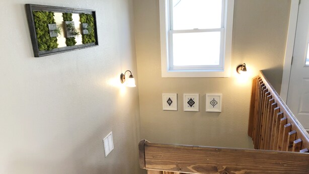 Een trap met houten leuningen, een wandlamp en drie kunstwerken in lijsten.