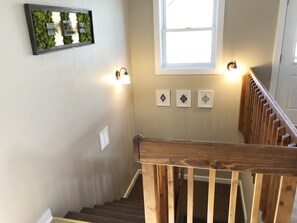 A staircase with wooden railings, a wall-mounted light fixture, and three framed wall art pieces.
