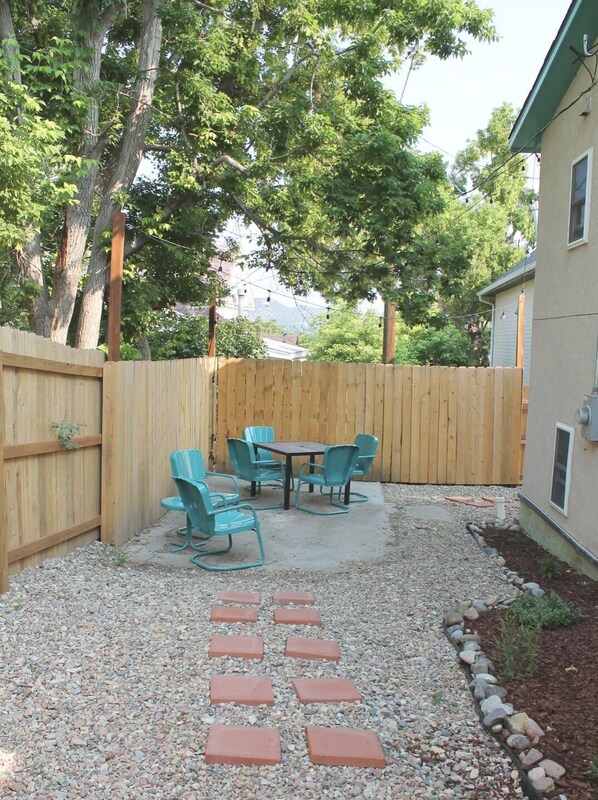 A backyard with a wooden fence, a gravel patio, and a table with chairs.