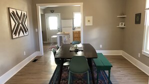 Een eetruimte met een donker houten tafel, groene stoelen en een kamerbreed tapijt. In de achtergrond is een keuken te zien.