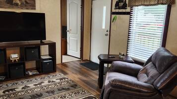 A living room with a leather sofa, a flat-screen TV, a patterned rug, and a door leading to another room.
