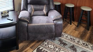 Una sala de estar con un sillón de cuero, una mesa de centro y una cocina con un lavamanos y taburetes.