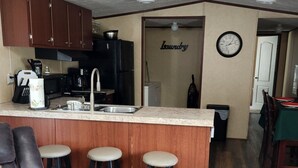 Un salón con un sofá de cuero marrón, un tapete estampado y una zona de cocina con armarios de madera y un lavamanos.