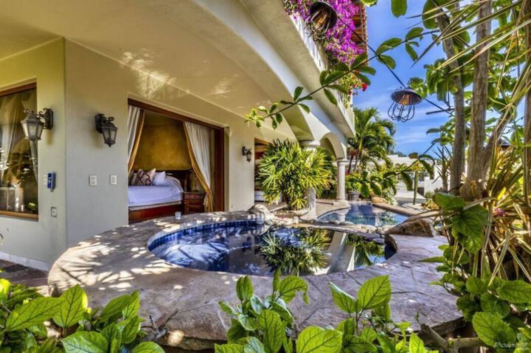 A hotel room with a curved pool, a bed, and a balcony with plants.