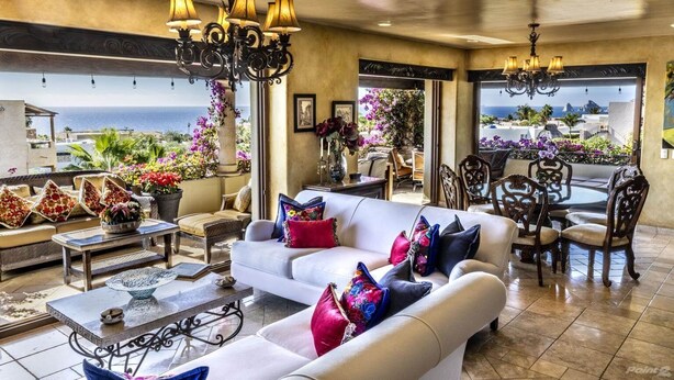 Ein geräumiges Wohnzimmer mit einem weißen Sofa, einem Esstisch und Stühlen. Mehrere Kronleuchter und Blick auf den Ozean durch große Fenster.