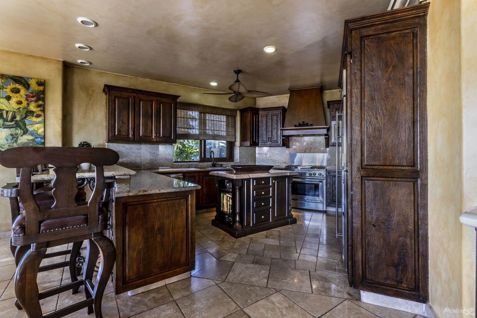 Une cuisine avec des meubles de rangement en bois foncé, un îlot central, une cuisinière et un ventilateur de plafond.