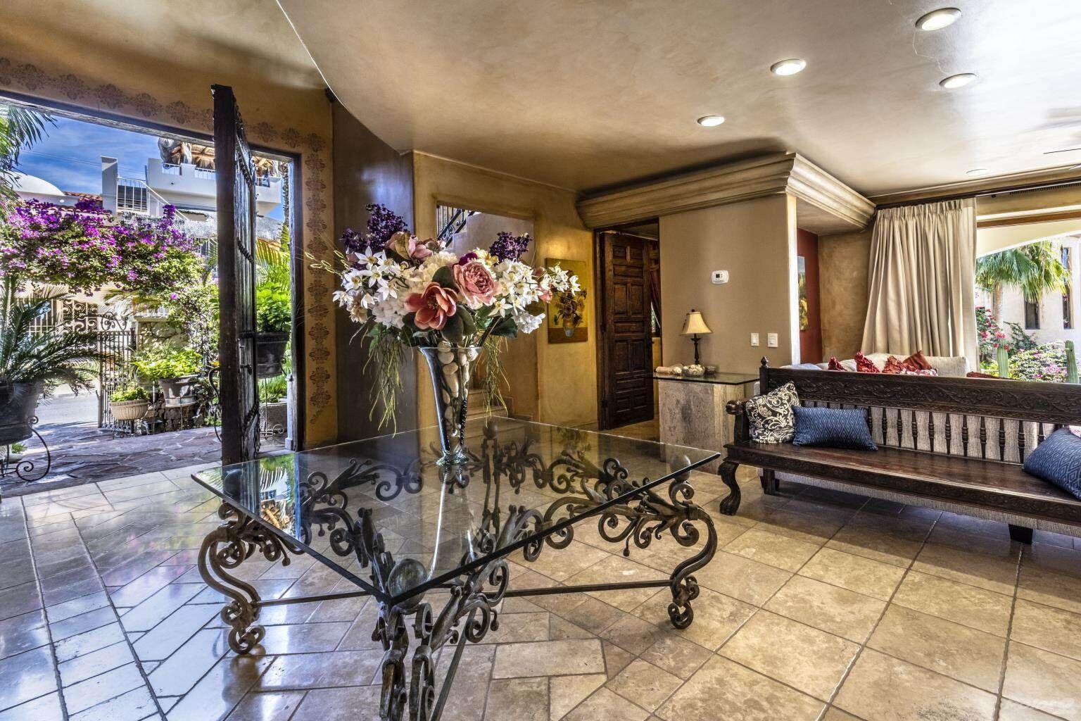 Eine Lobby mit einem Glastisch, einer Couch mit gemusterten Kissen und einer Blumenvase.