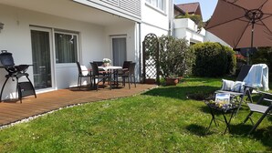 Eine Terrasse mit Tisch und Stühlen, einem Grill und einem Rasen.