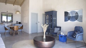 A spacious living area with a round coffee table, a blue armchair, and a dining area with a wooden table and chairs. - Casa Assisi with private pool & sea view (Kefalonia)