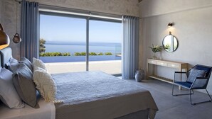 A bedroom with a large bed, a nightstand, a chair, and a view of the sea. - Casa Assisi with private pool & sea view (Kefalonia)