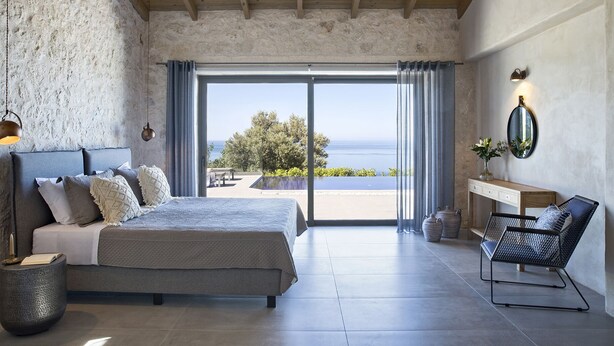 A bedroom with a bed, a chair, a nightstand, and a view of the sea. - Casa Assisi with private pool & sea view (Kefalonia)