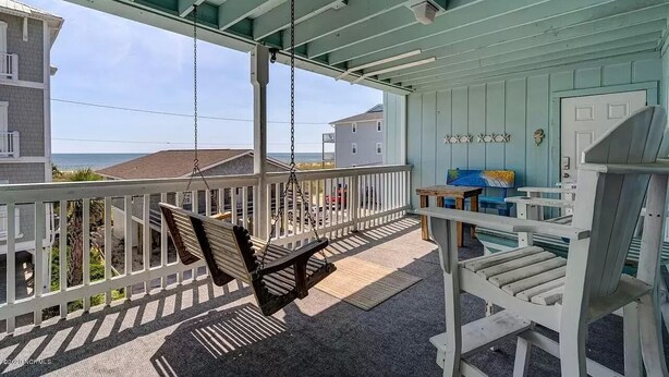 Un balcon abrité avec un fauteuil suspendu, une balustrade blanche et une vue sur l’océan.