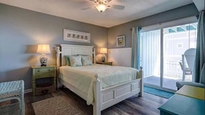 Une chambre à coucher avec un lit, deux tables de chevet avec des lampes, un ventilateur de plafond, une fenêtre avec des rideaux et une vue sur l’extérieur.