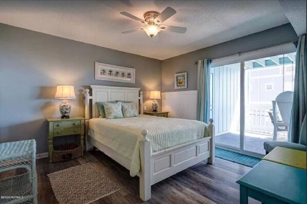 A bedroom with a bed, two bedside tables with lamps, a ceiling fan, a window with curtains, and a view of the outside. - Ocean & Lake Views. Steps to the Beach. (Carolina Beach)