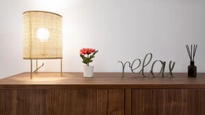 Ein Holztisch mit einer gewobenen Lampe, einem Topfpflanzen und einem dekorativen Schild mit der Aufschrift 'relax'.
