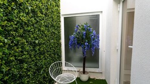 Ein kleiner Außenbereich mit einem weißen Stuhl, einem Blumentopf mit blauen Blüten und einer Glastür.