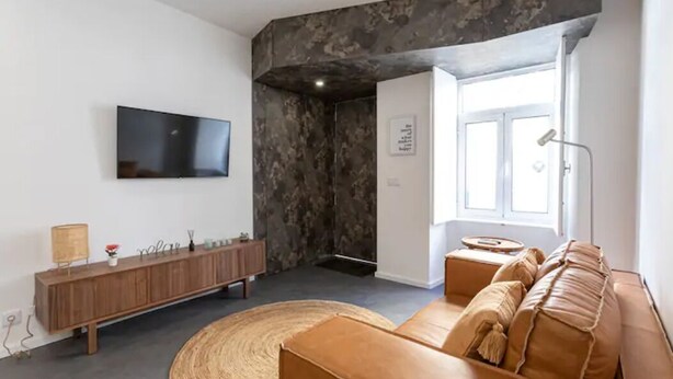 Ein modernes Wohnzimmer mit einem Flachbildfernseher, einer Holzkonsole, einem braunen Ledersofa und einem großen Webteppich.