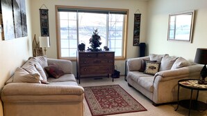 Un salon avec deux canapés beige, une commode en bois, un tapis à motifs rouges et une grande fenêtre donnant sur un paysage enneigé.