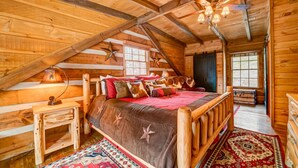 Un dormitorio de cabaña de troncos acogedor, con una cama grande, paredes de madera, una decoración de estrella y un ventilador de techo.