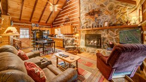 Interior acogedor de una cabaña de madera con chimenea de piedra, vigas de techo de madera y un rincón de comedor rústico.