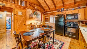 Interior de una cabaña de madera con comedor, cocina y una escalera que sube a un altillo.