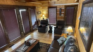 L’intérieur d’un chalet confortable, avec des murs en bois, un canapé en cuir, deux fauteuils, une table basse et un coussin décoratif à motifs d’ours.