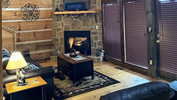 L’intérieur chaleureux d’un chalet avec une cheminée en pierre, des murs en bois, une tête d’ours servant de décoration et un téléviseur.