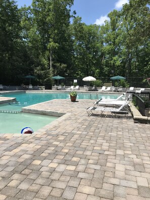 A pool area with lounge chairs and umbrellas, surrounded by trees.