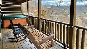 Une terrasse en bois avec un fauteuil suspendu et un fauteuil à bascule, un jacuzzi et une vue sur la ville.