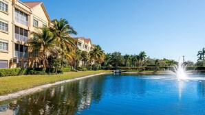 Une piscine avec une fontaine, entourée de palmiers et bordée d’un bâtiment doté de balcons.