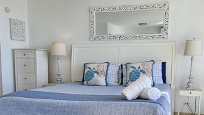 Un dormitorio con cama, dos mesitas de noche, un banco, un aparador y un espejo.