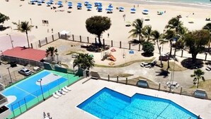 Un área de piscina con cancha de baloncesto, sillones de descanso y palmeras.