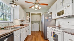 A kitchen with white cabinets, a stainless steel dishwasher, a refrigerator, a microwave, and a stove. - Beach View Cottage Perfect for Family & Friends! (Gulfport)