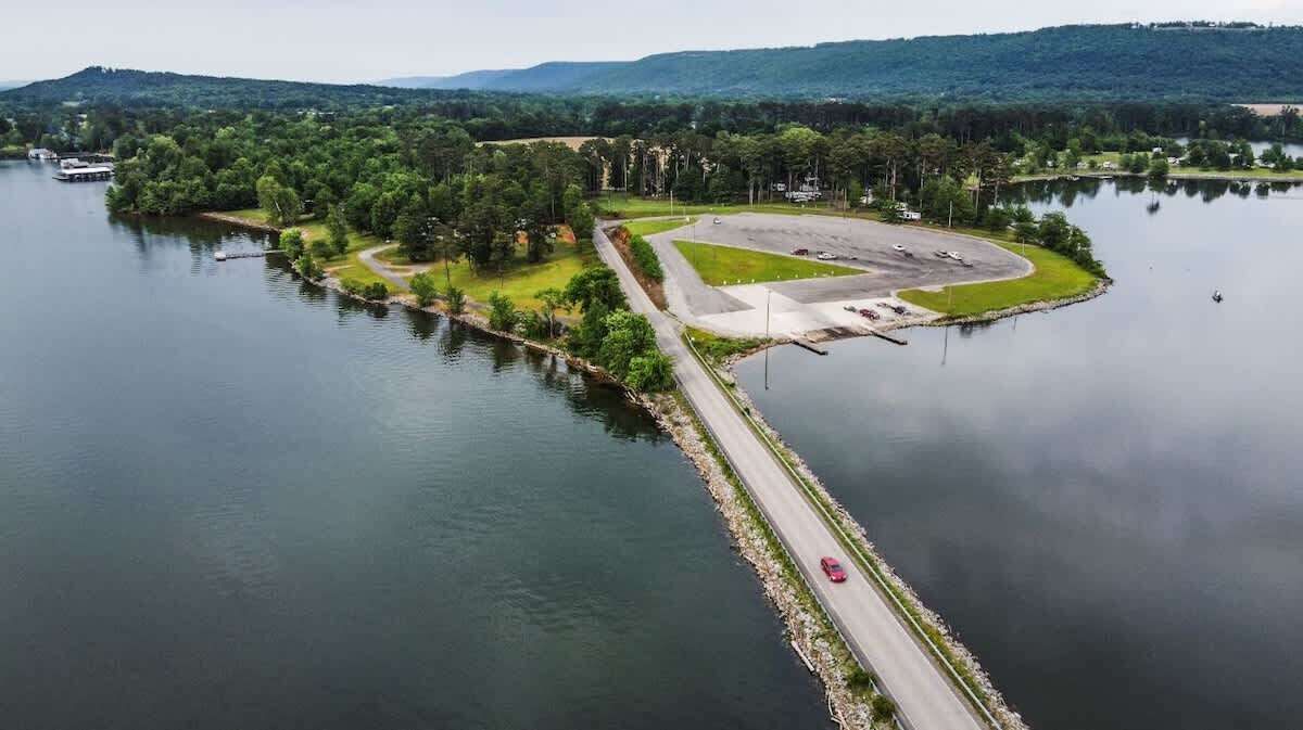 Vue aérienne d’une propriété au bord d’un lac, avec une route, des zones herbeuses et un parking.