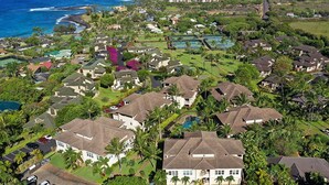 An aerial view of a residential area with houses, a large swimming pool, and a view of the ocean. - Poipu Kai B111: Lovely Gardenview Villa w/Shared Pool, Spa & AC, Near Beaches (Koloa)