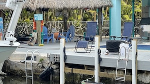 A dock with a small boat, lounge chairs, and a thatched-roof structure. - The most setup home in BPK TIKI HUT,POOL ,GRILL ,CANAL FRONT, FREE UNLIMITED ICE (Gordon road)