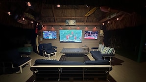 An outdoor cinema with a thatched roof, multiple screens, and comfortable seating. - The most setup home in BPK TIKI HUT,POOL ,GRILL ,CANAL FRONT, FREE UNLIMITED ICE (Gordon road)