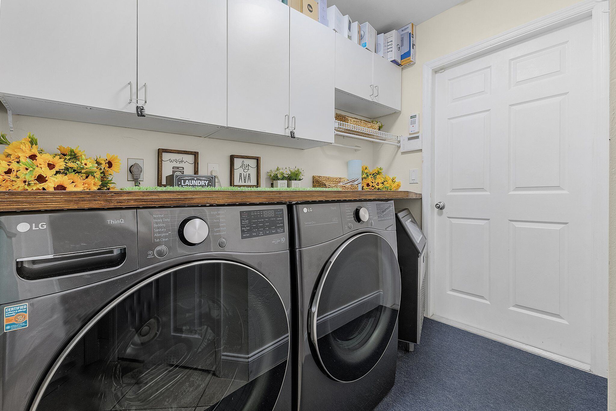 Une buanderie équipée de deux lave-linge à chargement frontal LG ThinQ, de meubles blancs et d’une porte blanche.
