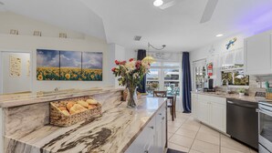 A modern kitchen with a marble countertop, a built-in oven, and a dishwasher. There is a vase with flowers on the counter, and a basket of bread. - Stunning Waterfront Oasis - Bikes, Kayaks, Pool & Spa, and much more! - Villa X-Ta-Sea - Roelens (Cape Coral)